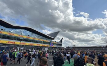 Fans running down main straight at Silverstone towards podium, with a blue cloudy sky above.