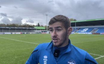 Eastleigh player standing on the pitch wearing a blue jacket