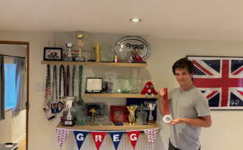 Wheelchair tennis player Greg Slade holding his Paralympic silver medal to the right, next to three shelves of accolades.