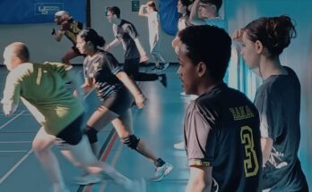 Dodgeball players running to the left of a sports hall.