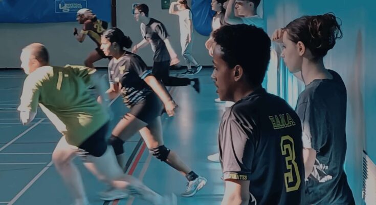 Dodgeball players running to the left of a sports hall.