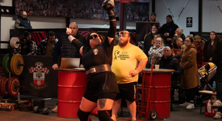 Women's Strongman Competitor lifts dumbbell over head