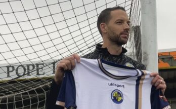 Aaron Martin is holding a Havant & Waterlooville shirt, leaning against a goalpost.