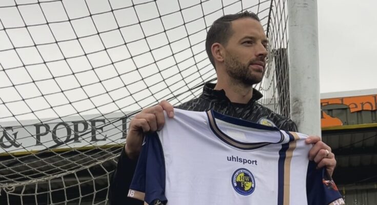 Aaron Martin is holding a Havant & Waterlooville shirt, leaning against a goalpost.