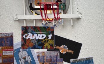 A basketball mini hoop is on a white wall covered in brand images and posters