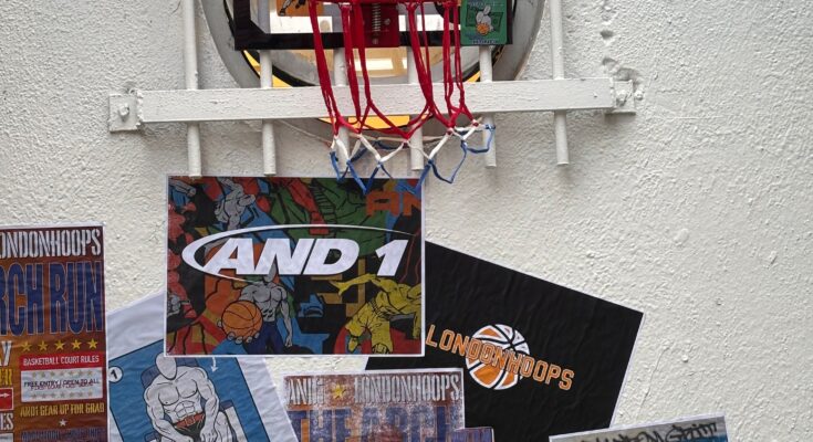 A basketball mini hoop is on a white wall covered in brand images and posters
