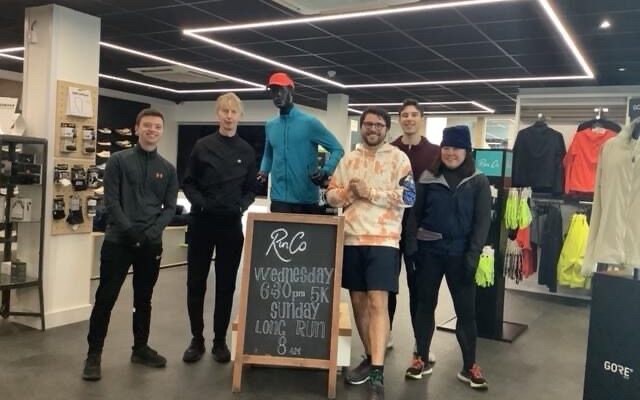 Five people stood in a run shop around a sign