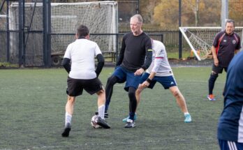 A walking football player shields the ball away from a defender trying to tackle him.