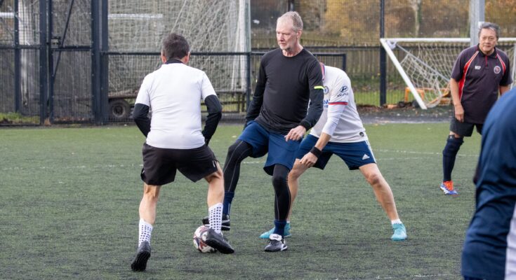 A walking football player shields the ball away from a defender trying to tackle him.