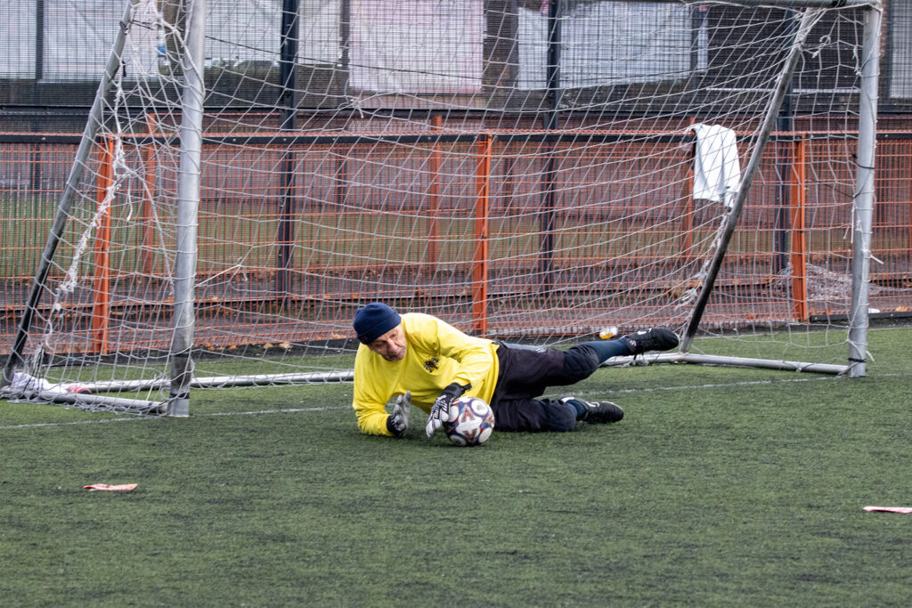 Walking football goalkeeper dives to retrieve the ball.