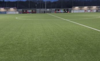 A small football stadium in the evening with a floodlight on in the background