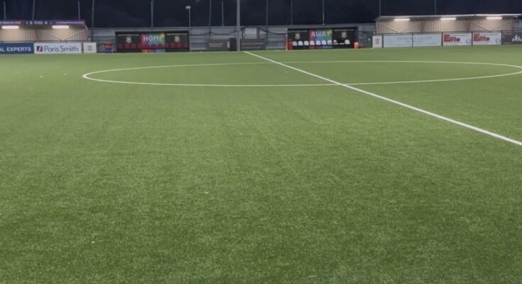 A small football stadium in the evening with a floodlight on in the background