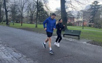 Two people running through a wet park park under a grey winter sky