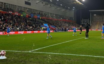 Women's football players stand on pitch for throw in.