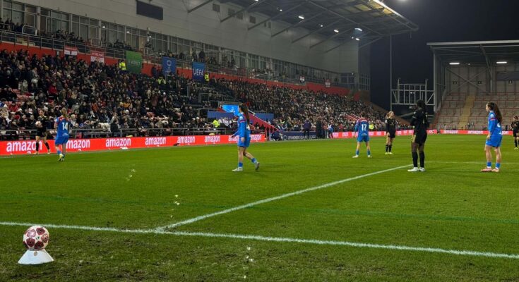 Women's football players stand on pitch for throw in.