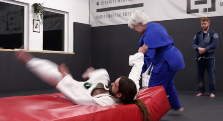 Judoka Leah Cozens throws another participant onto a red mat whilst learning.