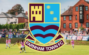 The badge of Farnham Town with the background of their stadium