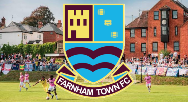 The badge of Farnham Town with the background of their stadium
