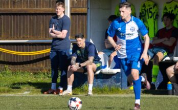 Christchurch player running to ball with Christchurch coaches stood and sat behind him.