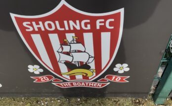 Red and White badge on a black background on a fence