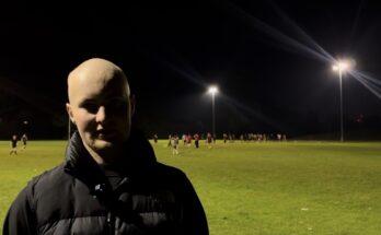 A man stood in the foreground with rugby being played in the background.