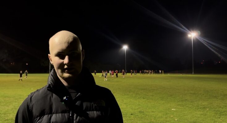 A man stood in the foreground with rugby being played in the background.