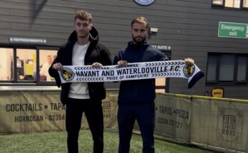 Two football managers holding a scarf on a football pitch.