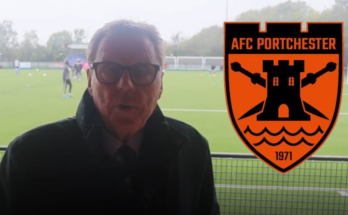 A man with glasses and brown hair looks at a camera with a football pitch in the background and the badge of AFC Portchester to the right